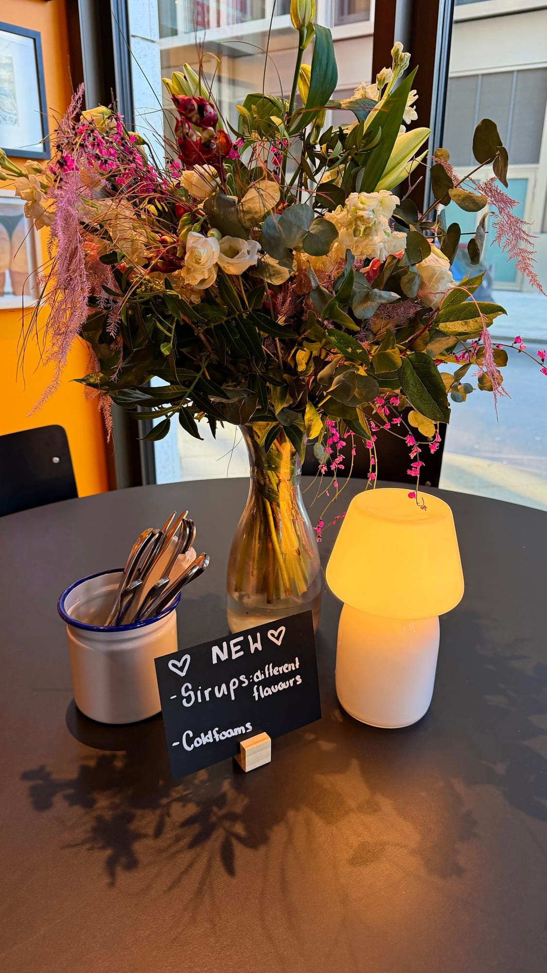 Table with flowers, a lamp and a sign for new syrups