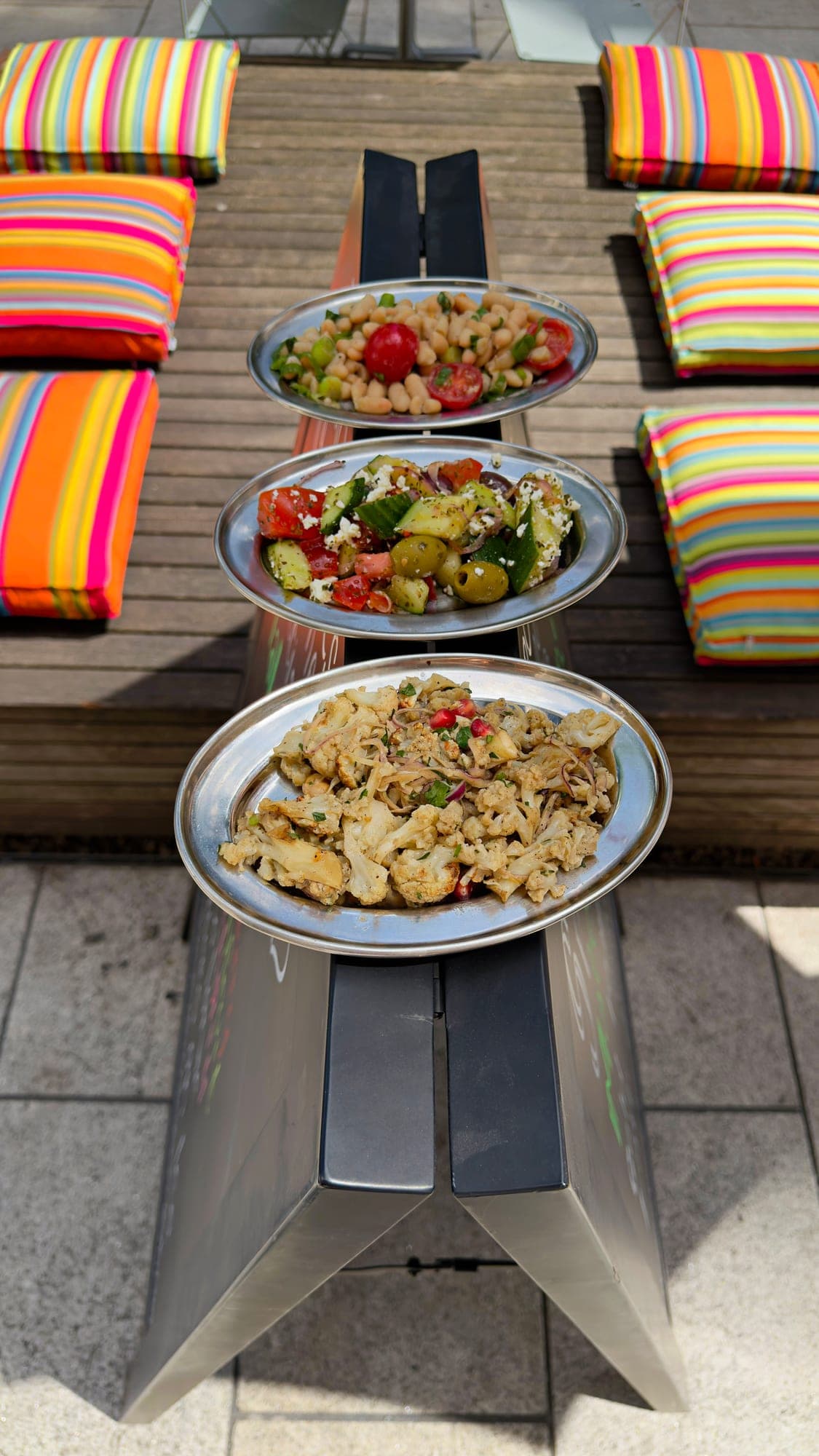 Three salads on a bench between colourful cushions