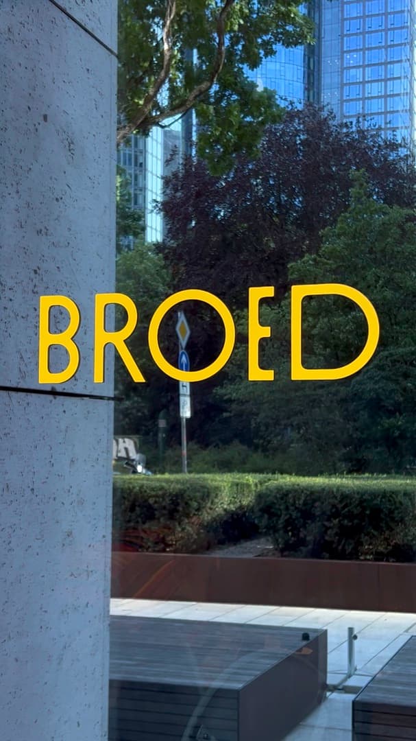 Yellow BROED lettering on the window, trees and towers behind
